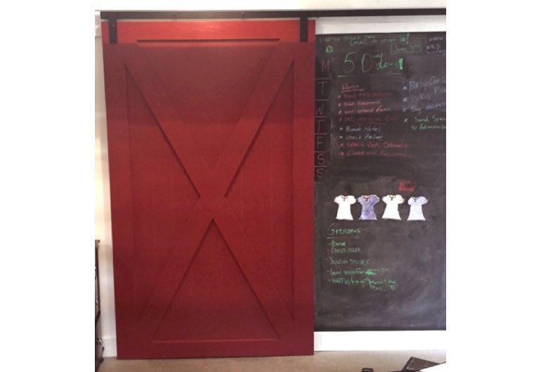 Red x-frame barn door with black hardware next to chalkboard 